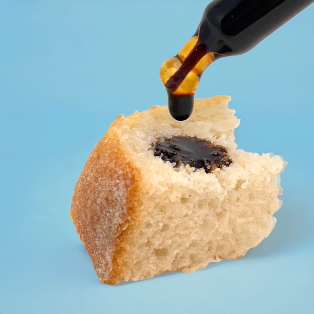 Das Bild zeigt ein Stück trockenes Brot, auf dieses mit einer Pipette 2 Tropfen tiefschwarzer Tinktur getropft wird